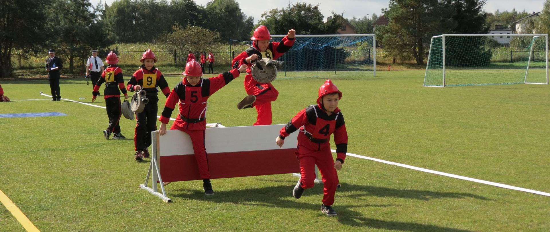 Zdjęcie przedstawia młodych zawodników drużyny MDP pokonujących płotek podczas konkurencji rozwinięcia bojowego.