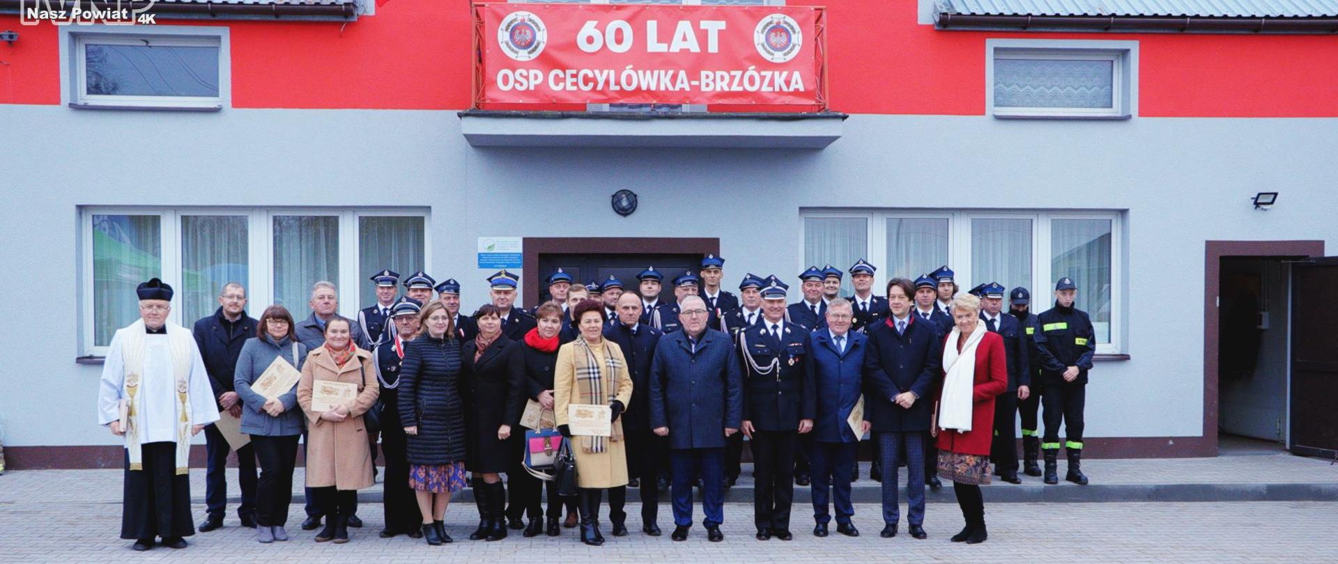 goście zaproszeni, druhowie OSP pozują do zdjęcia stojąc przed remizą strażacką 