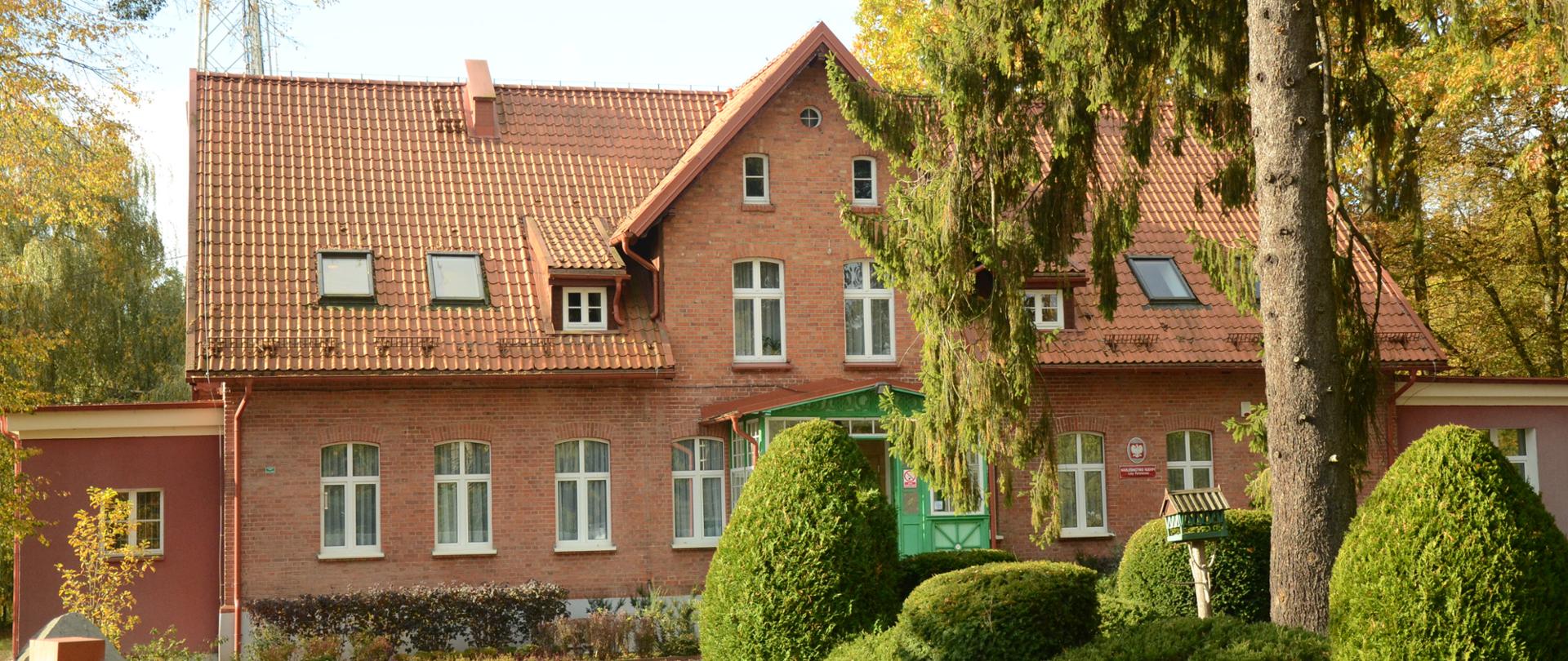 Teren siedziby Nadleśnictwa Kudypy, ceglany budynek biurowy z zielonym gankiem.