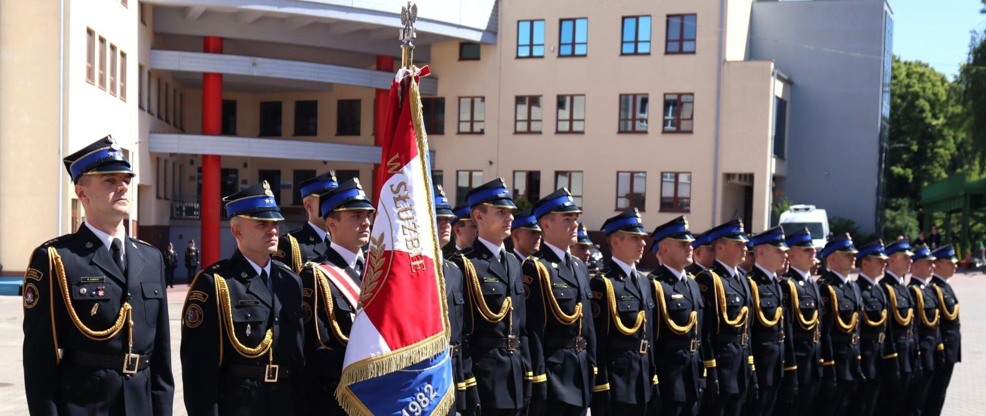 Poczet sztandarowy oraz kompania reprezentacyjna stoją na palcu wewnętrznym Akademii Pożarniczej podczas uroczystego apelu z okazji dnia strażaka.