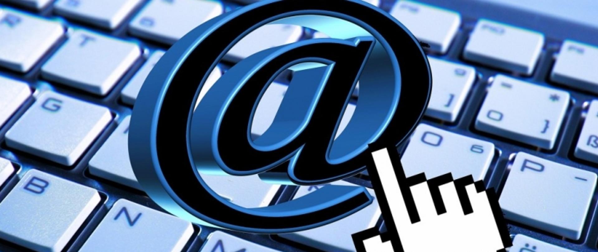 Symbol „@” na tle klawiatury komputerowej z kursorem w formie dłoni.