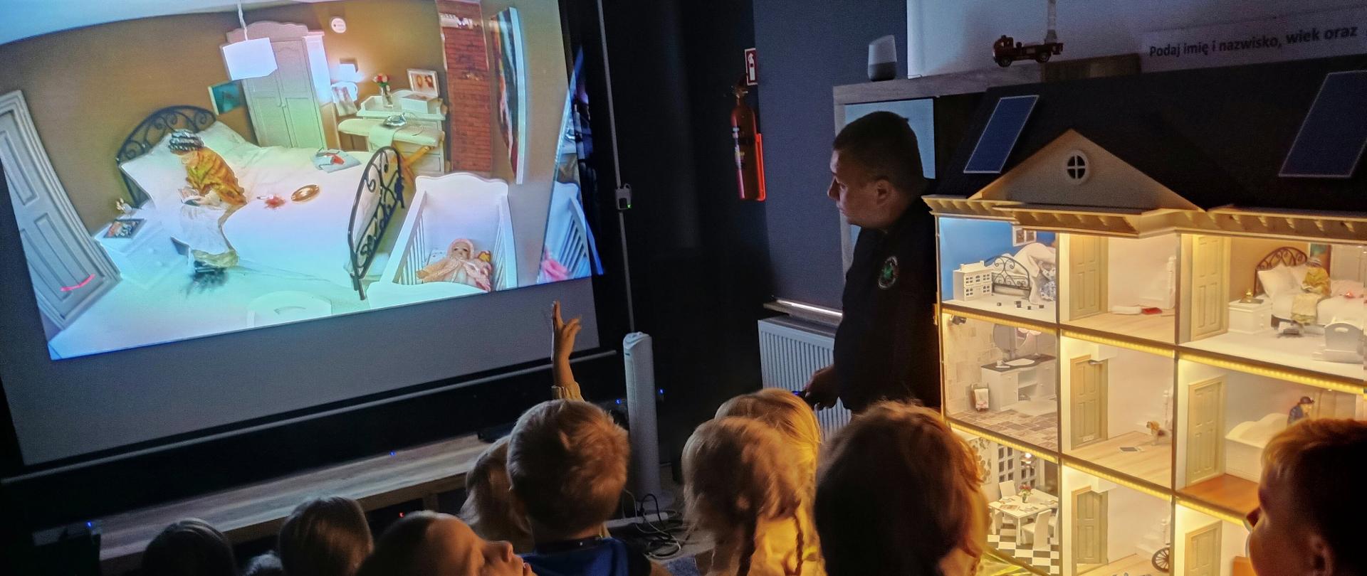 Dzieci w sali edukacyjne stoją przy domku szkoleniowym.