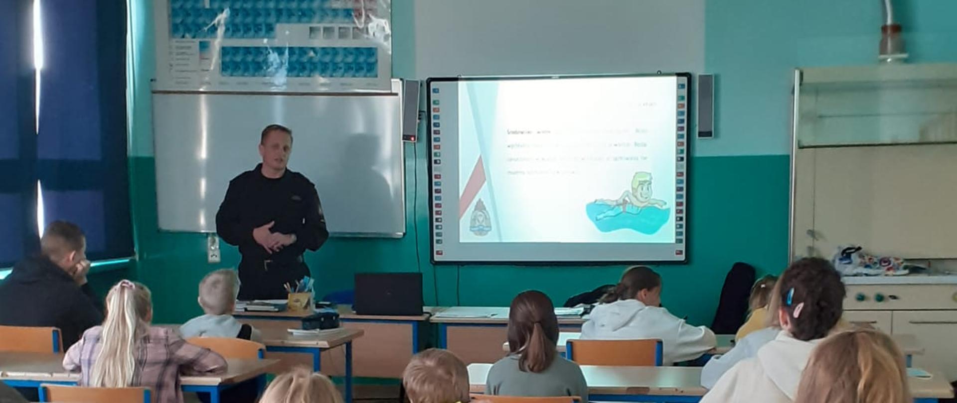 Na zdjęciu znajduje się klasa uczniów oraz strażak podczas prelekcji