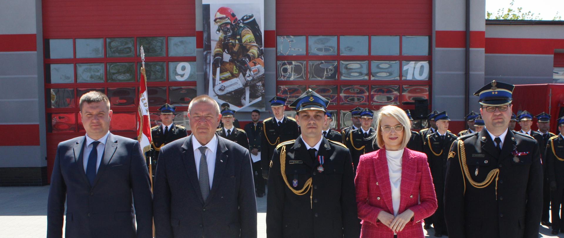 zdjecie grupowe strażaków , posłów na tle budynku komendy 