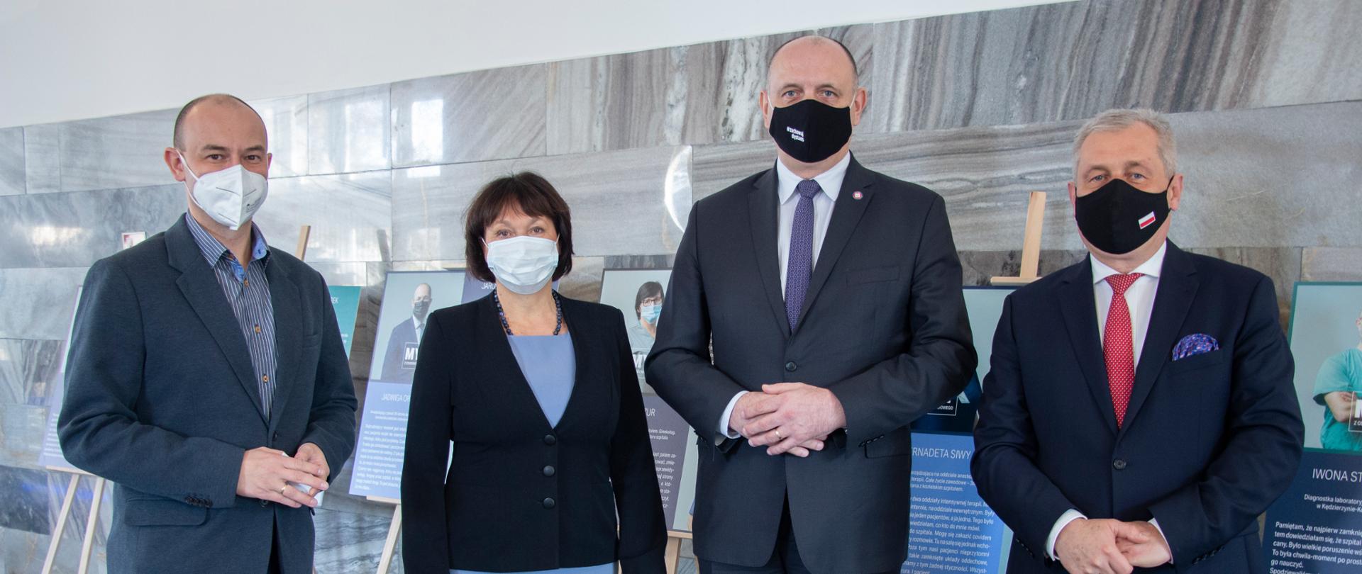 Na zdjęciu cztery osoby. Od lewej współtwórca wystawy Adam Liszka. Obok dyrektor WSSE Opole, Główny Inspektor Sanitarny oraz Wojewoda Opolski. W tle plansze wystawy. 