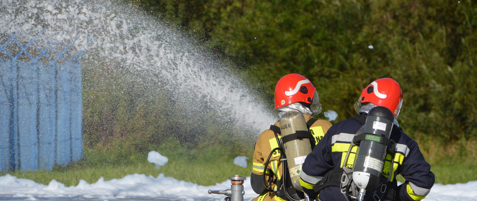 Fotografia przedstawia strażaków podających pianę na pożar podczas ćwiczeń.