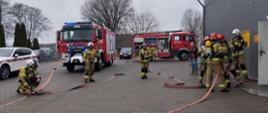 Na zdjęciu samochody strażackie oraz grupa strażaków z linią gaśniczą wchodzi na magazyn.