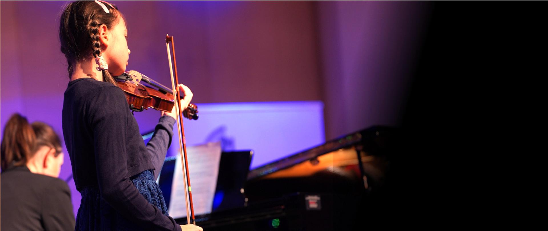 Grafika przedstawia dziewczynkę grającą na skrzypcach na tle fortepianu
