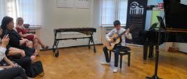 Zdjęcie przedstawia ucznia grającego na gitarze podczas koncertu absolwentów.