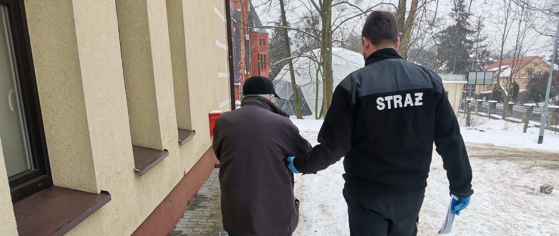 Na zdjęciu strażak prowadzący mężczyznę do punktu szczepień