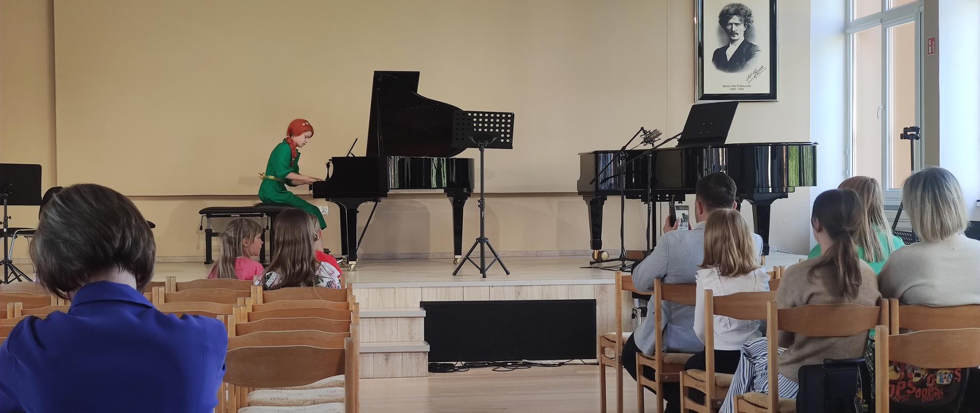 uczennica grająca na fortepianie, na widowni siedzący słuchacze