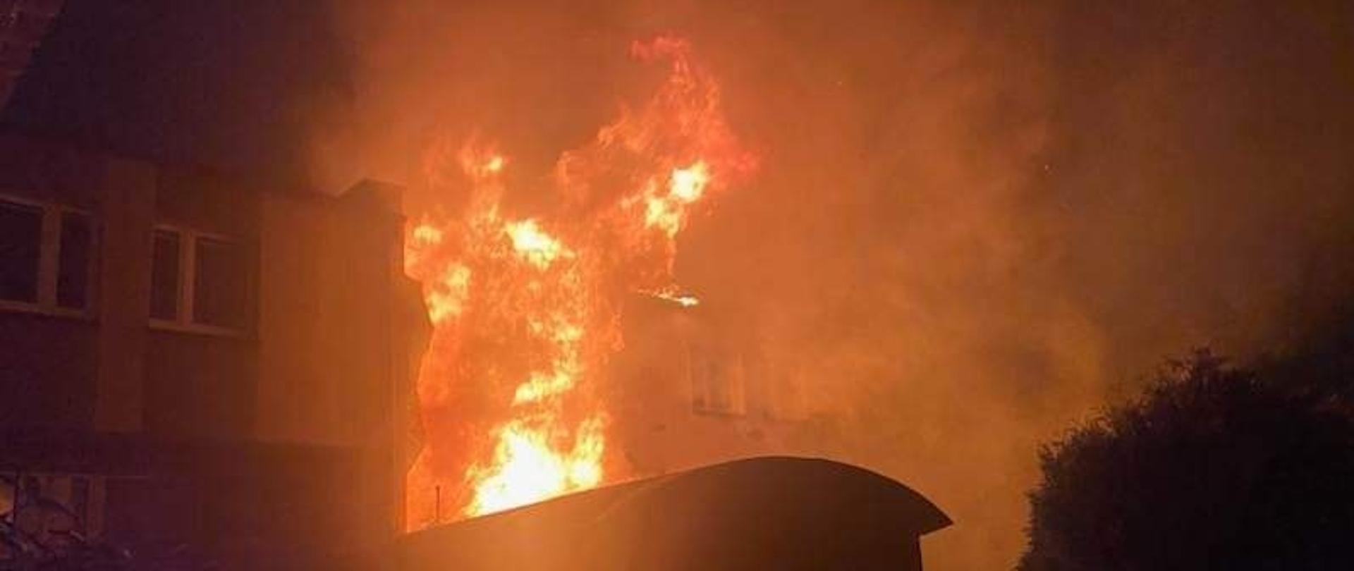 Widać budynek mieszkalny cały objęty ogniem, jest noc