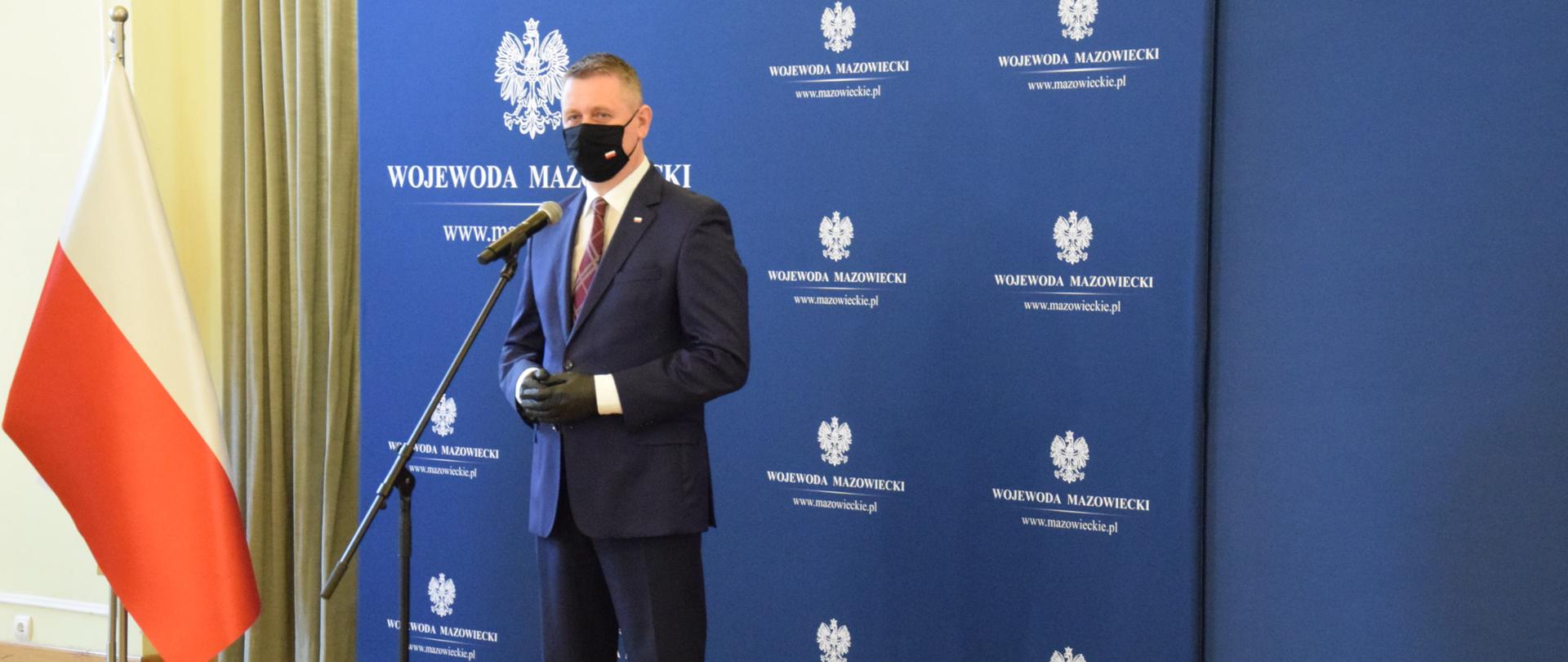 Na zdjęciu stoi mężczyzna mówiący do mikrofonu