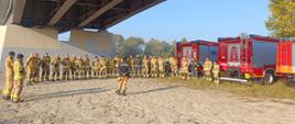 Zbiórka na miejscu ćwiczeń podczas której dowódca przekazuje założenia ćwiczeń. W tle samochody pożarnicze.