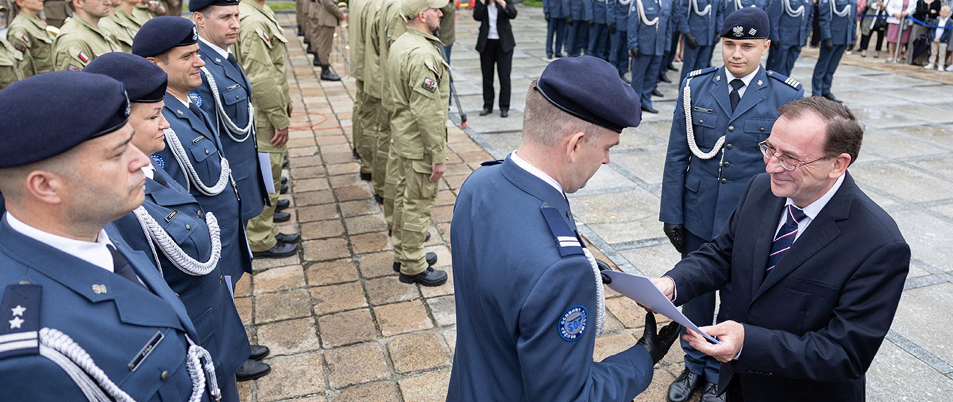 Na zdjęciu widać ministra Mariusza Kamińskiego wręczającego akt promocji na wyższy stopień.