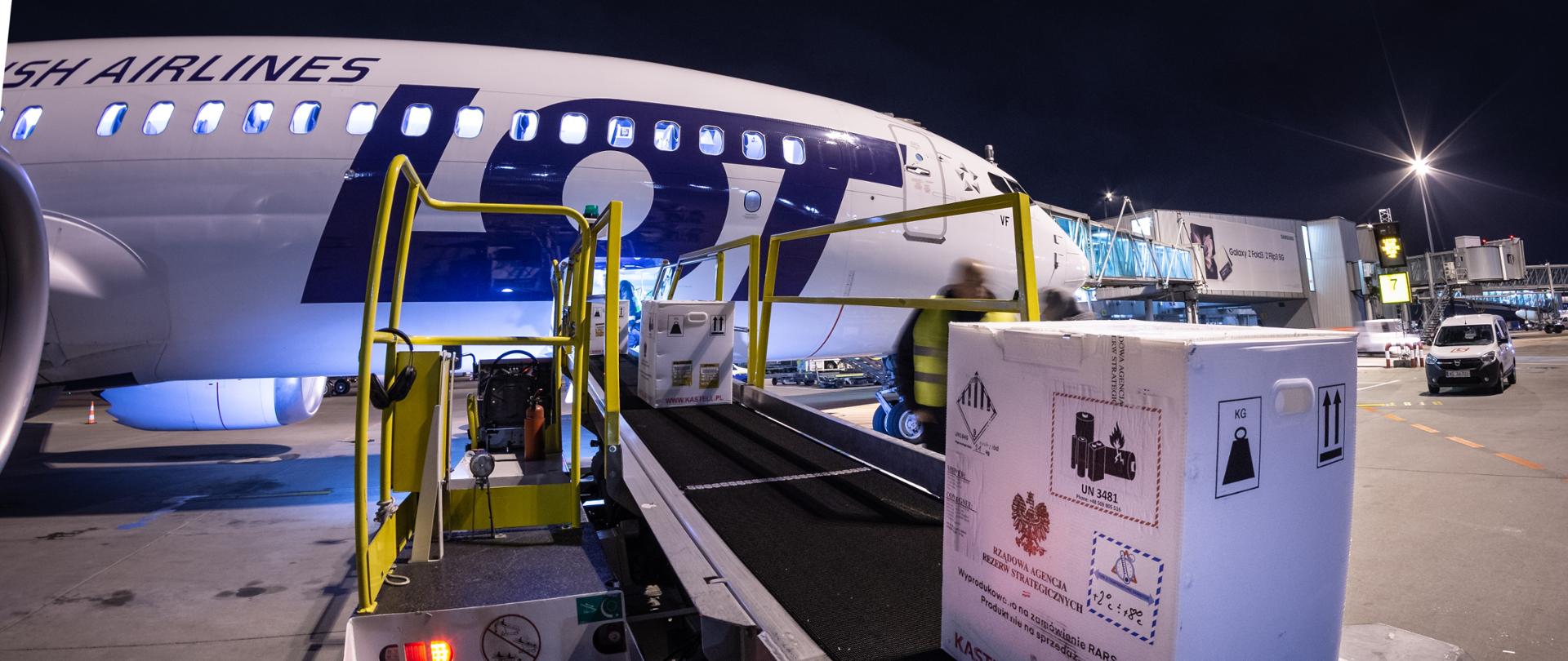 Duże paczki są wiezione na taśmie transportowej do samolotu z napisem LOT