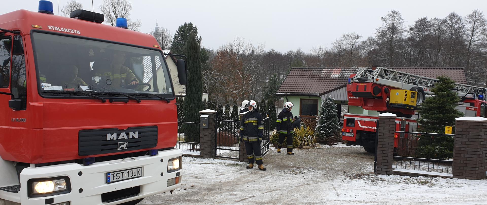Samochody pożarnicze GCBA , SD-23 oraz dwóch ratowników OSP na posesji przed uszkodzonym w wyniku pożaru budynkiem, pora dzienna mała pokrywa śniegu.