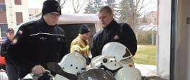 Sprzęt pożarniczy dla ukraińskich strażaków. Komenda Powiatowa PSP w Rawiczu. Strażacy przygotowują do transportu zebrany sprzęt. Na europalecie układają hełmy strażackie, które następnie będą owijać folią. W tle przyczepka i fragment budynku komendy.