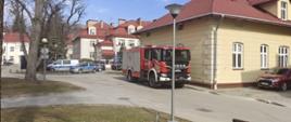 Na zdjęciu widoczny jest samochód ratowniczo-gaśniczy stojący na terenie centrum medycznego w Łańcucie podczas ćwiczeń. dalej stoją dwa radiowozy policji. Wokół jest ogrodzony teren taśmą policyjną.