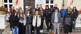 Grupa uczniów wraz z opiekunem pozuje do wspólnego zdjęcia przed budynkiem Stadniny Koni Białka
