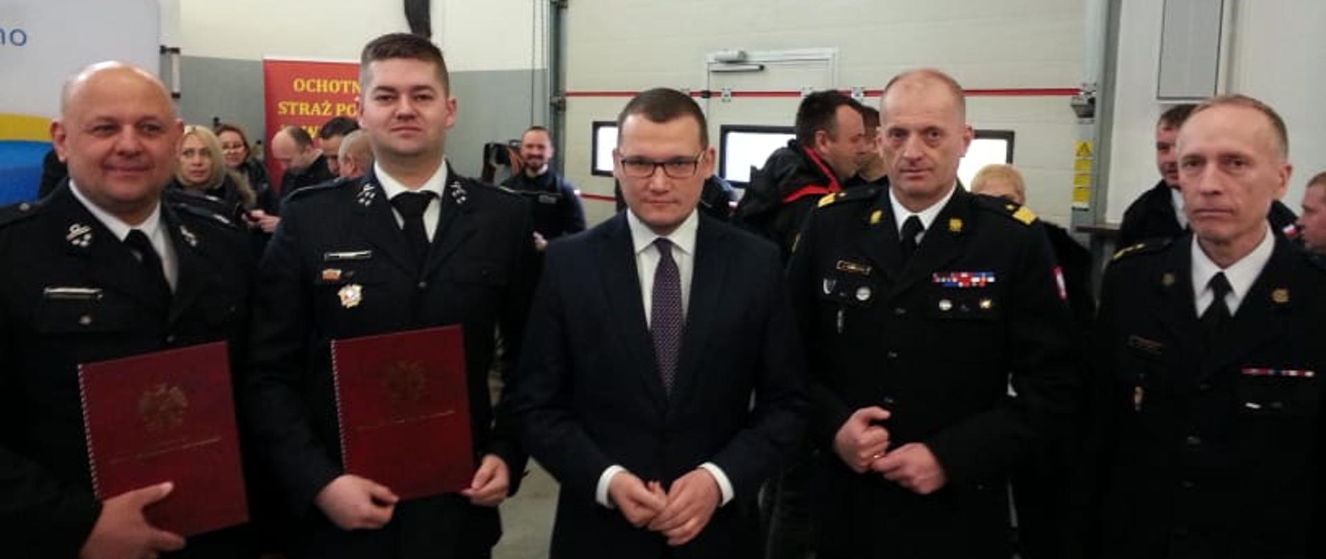 Zdjęcie przedstawia wręczanie symboliczne decyzji na zakup nowych wozów. Ma to miejsce w garażu OSP.