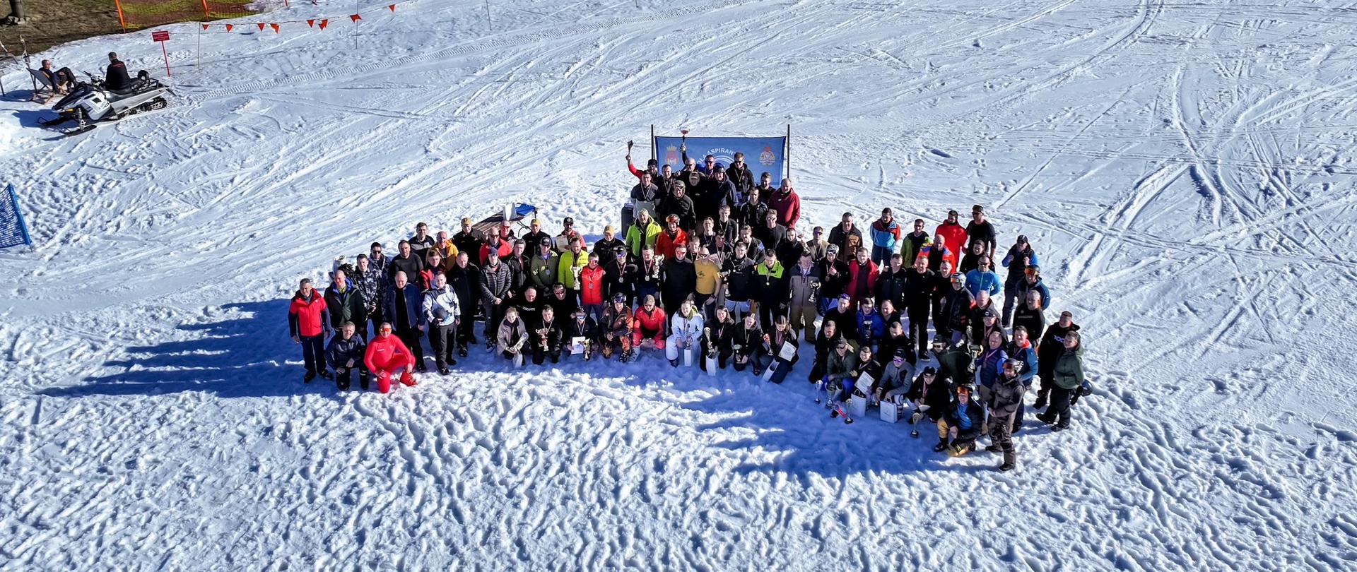Zdjęcie z drona przedstawiające dużą grupę strażaków i uczestników zawodów zgromadzonych na stoku narciarskim podczas wspólnego zdjęcia po zakończeniu rywalizacji
