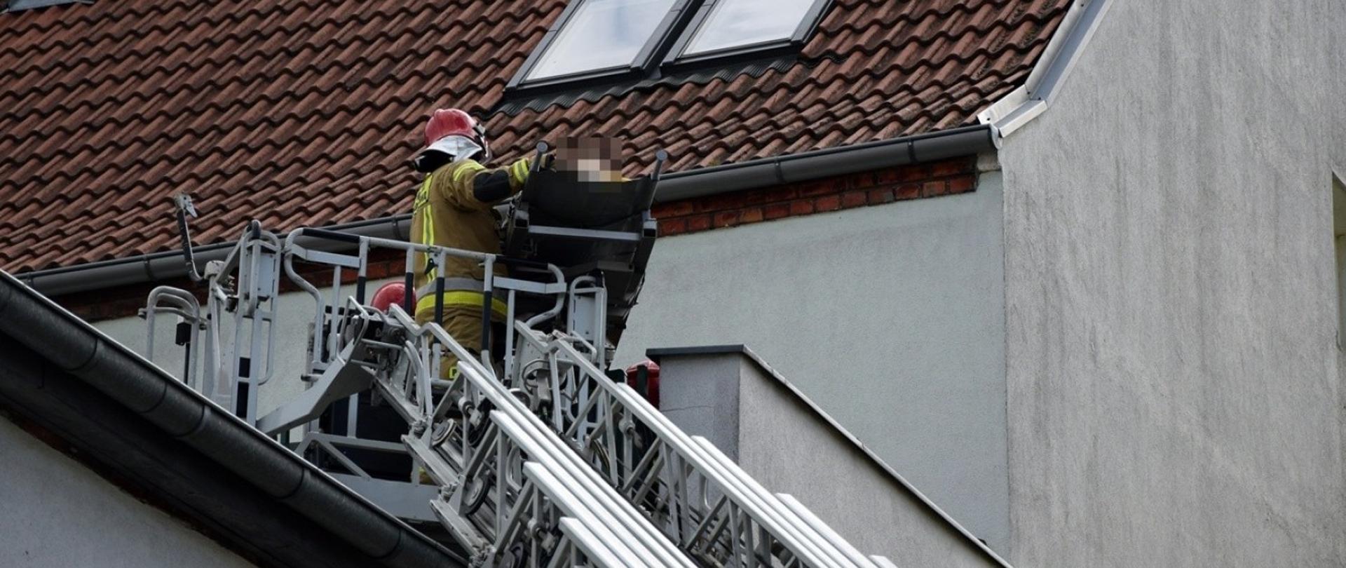 Strażacy wkładają nosze z poszkodowaną na kosz drabiny mechanicznej