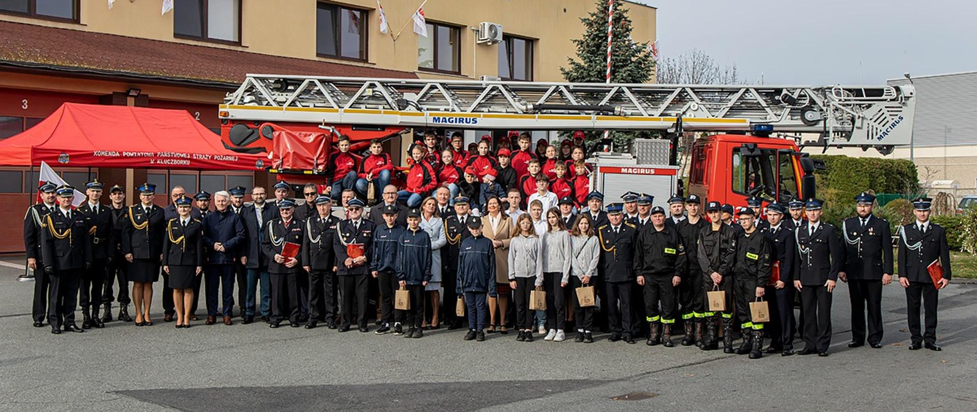 Wspólne zdjęcie uczestników uroczystości w KP PSP w Kluczborku. W tle widoczna drabina mechaniczna.