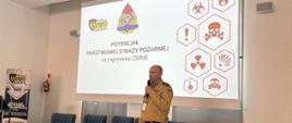 Strażak z mikrofonem prowadzący szkolenie w tle slajd wyświetlony na ścianie 