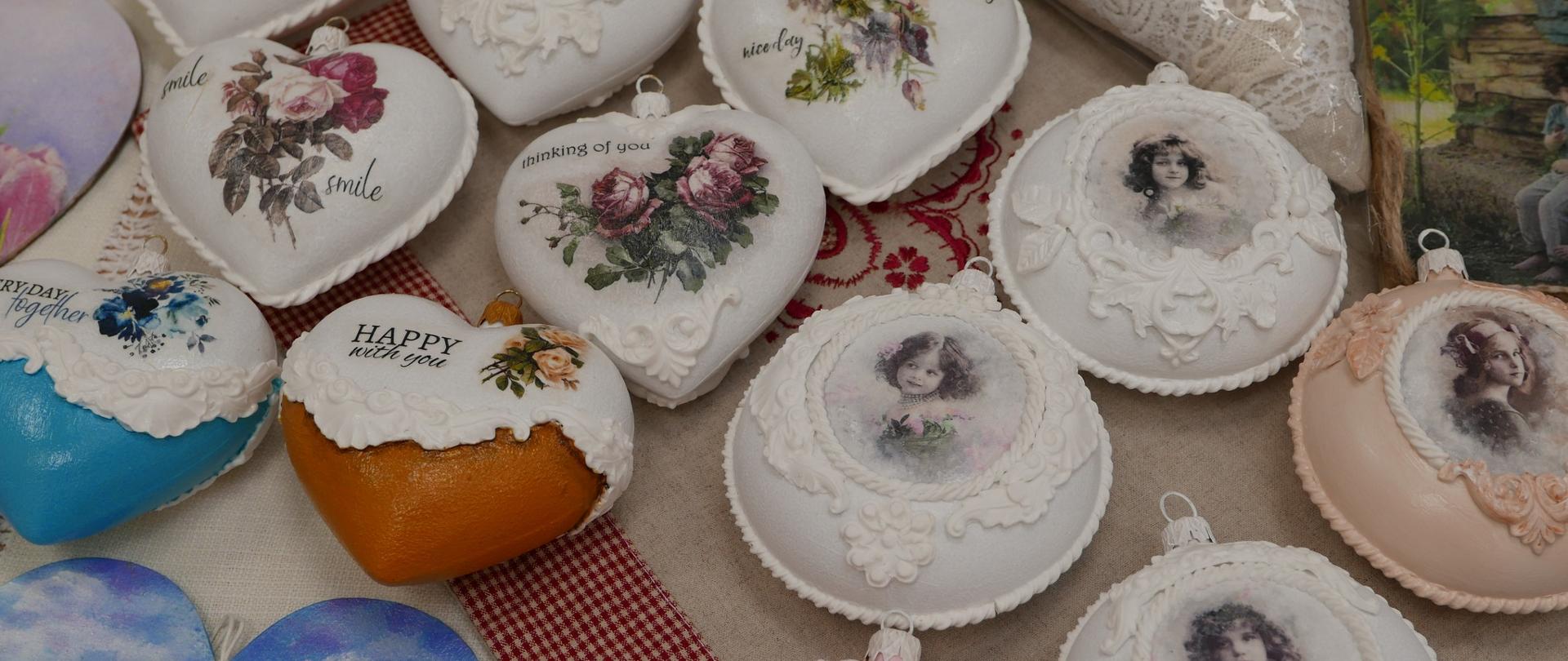 Białe bombki w kształcie serc z namalowanymi kwiatami leżą na serwecie a obok nich po prawej stronie bombki ze starymi portretami dzieci