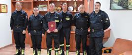 Na zdjęciu widać sześciu strażaków stojących w szeregu , jeden z nich trzyma w dłoniach bordową teczkę- to obchodzący jubileusz 20 lecia służby i pracy st. str. Jakub Dolecki.