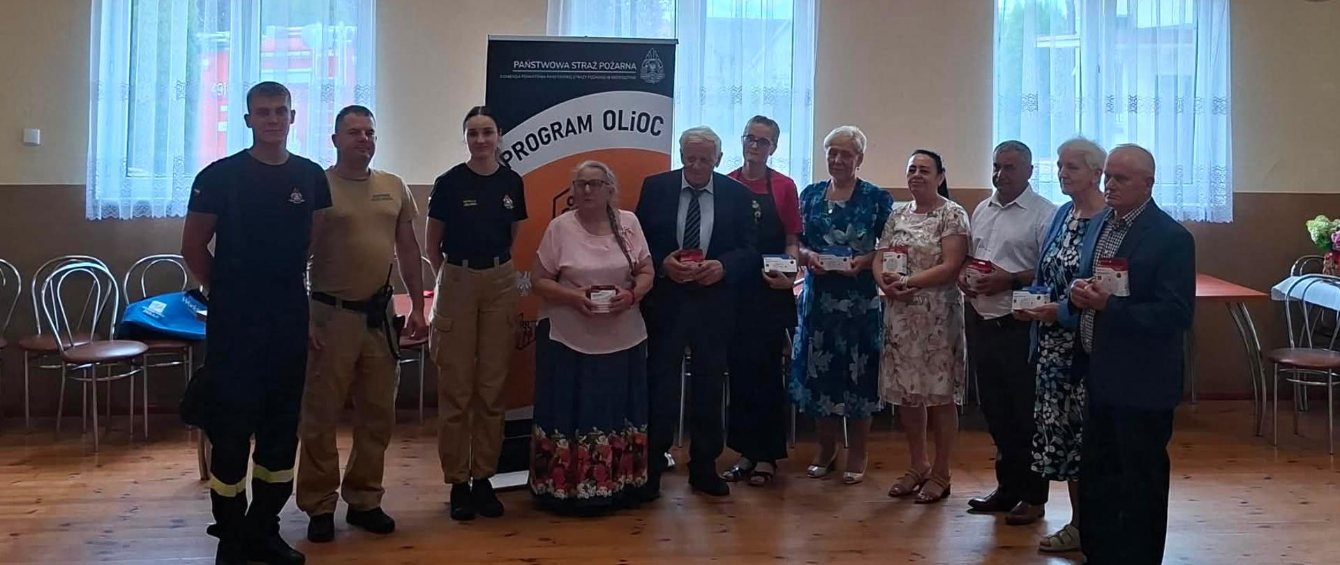 Na zdjęciu widać funkcjonariuszy PSP oraz seniorów z czujkami podczas spotkania edukacyjnego.
