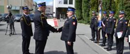 Zastępca Podkarpackiego Komendanta Wojewódzkiego PSP wręcza dyplom wyróżnionemu strażakowi asp. sztab. Bogdanowi Świętoniowi w asyście Starosty i Komendanta Powiatowego w tle strażacy na zbiórce