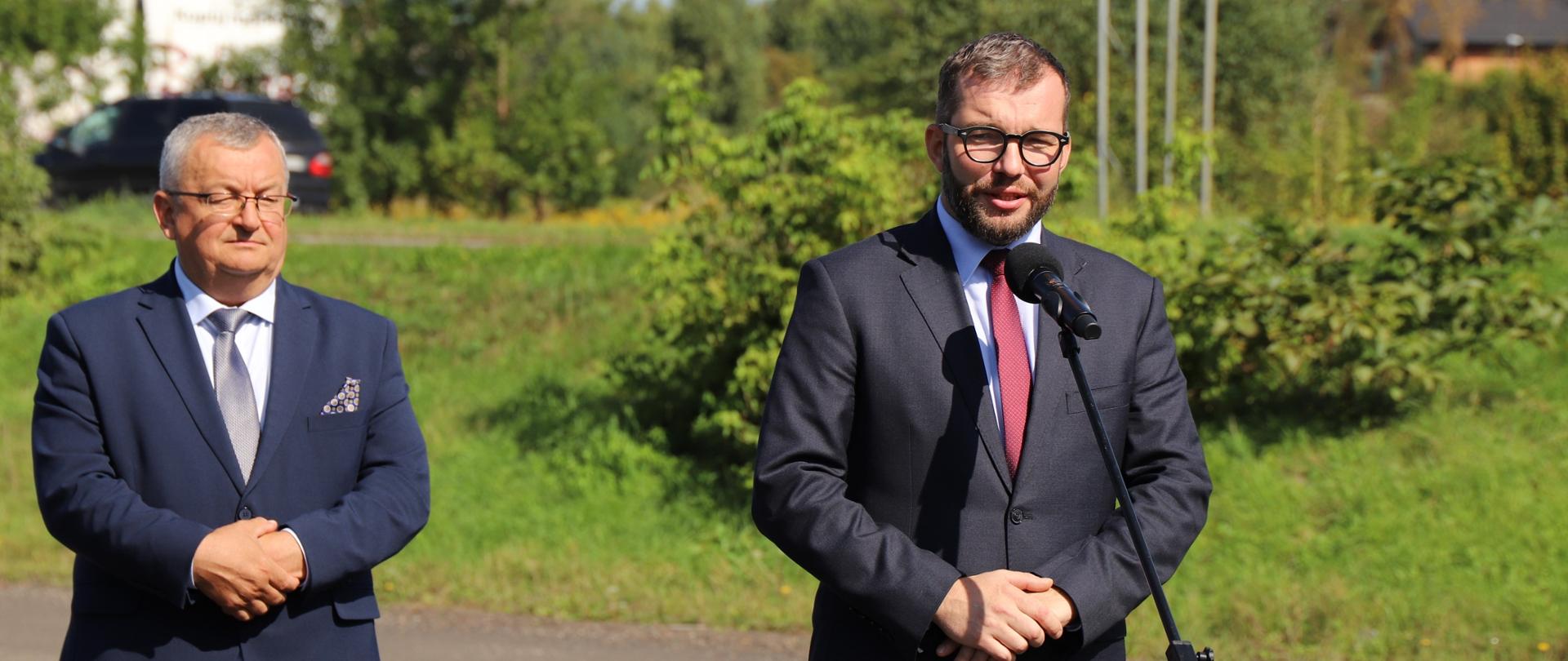 Minister Puda stoi przy mikrofonie za nim stoi minister Adamczyk 