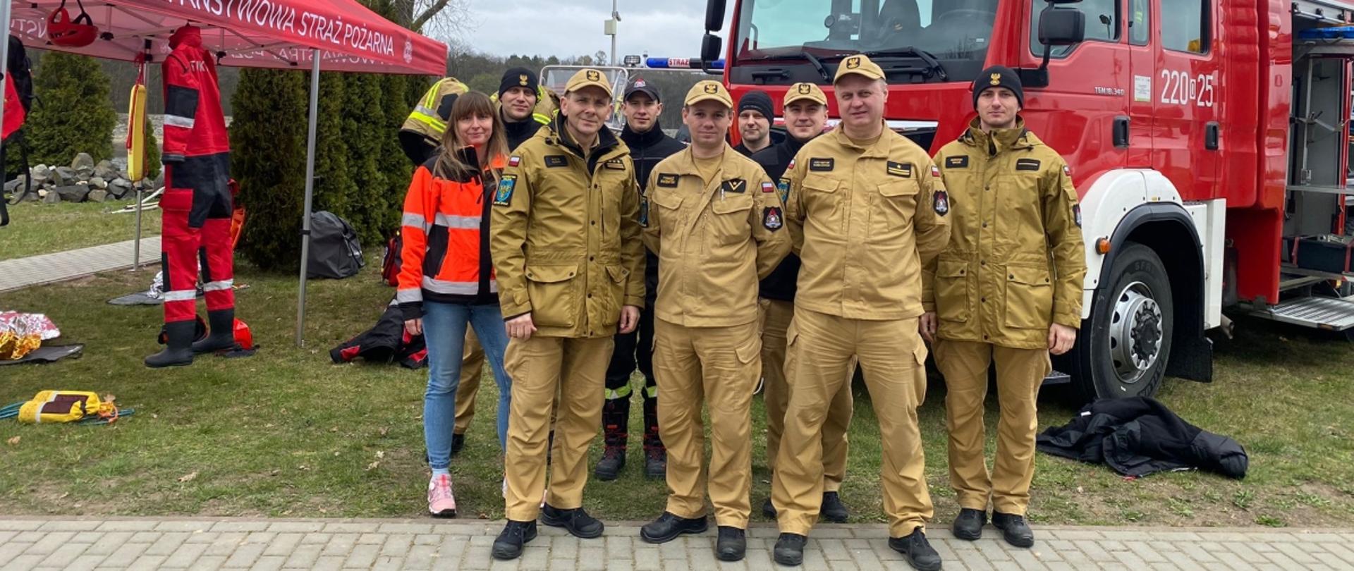 Wspólne zdjęcie strażaków i pracownicy PSP z Zastępcą Opolskiego Komendanta Wojewódzkiego PSP st. bryg. Piotrem Dudkiem na tle stanowisk dydaktycznych pikniku z okazji Światowego Dnia Wody w Turawie.