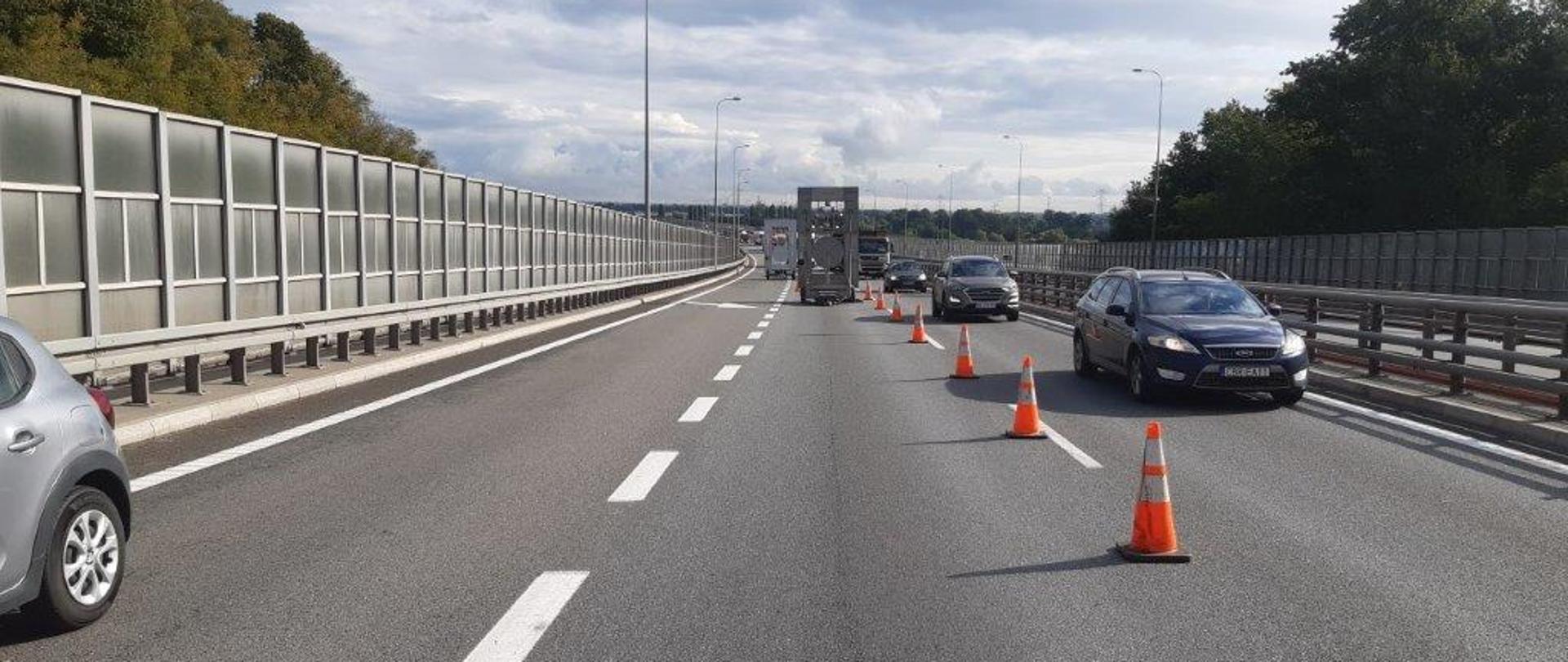 Widok na drogę ekspresową S7 Południową Obwodnicę Gdańska. Widoczne zwężenie jezdni, ustawione pachołki i znak ostrzegający o zwężeniu. Samochody są kierowane na tzw. szybki pas w kierunku Obwodnicy Trójmiasta.