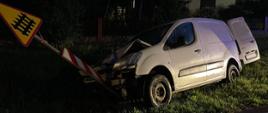 Zdjęcie przedstawia rozbity samochód Citroen Berlingo koloru białego. Pojazd stoi na pasie zieleni przy drodze. Uszkodzeniu uległ pionowy znak drogowy na który wjechał pojazd. 