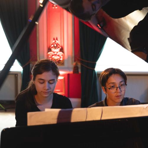 zdjęcie przedstawia dwoje uczniów grających w duecie na fortepianie, ujęcie od przodu pod podniesionym skrzydłem fortepianu