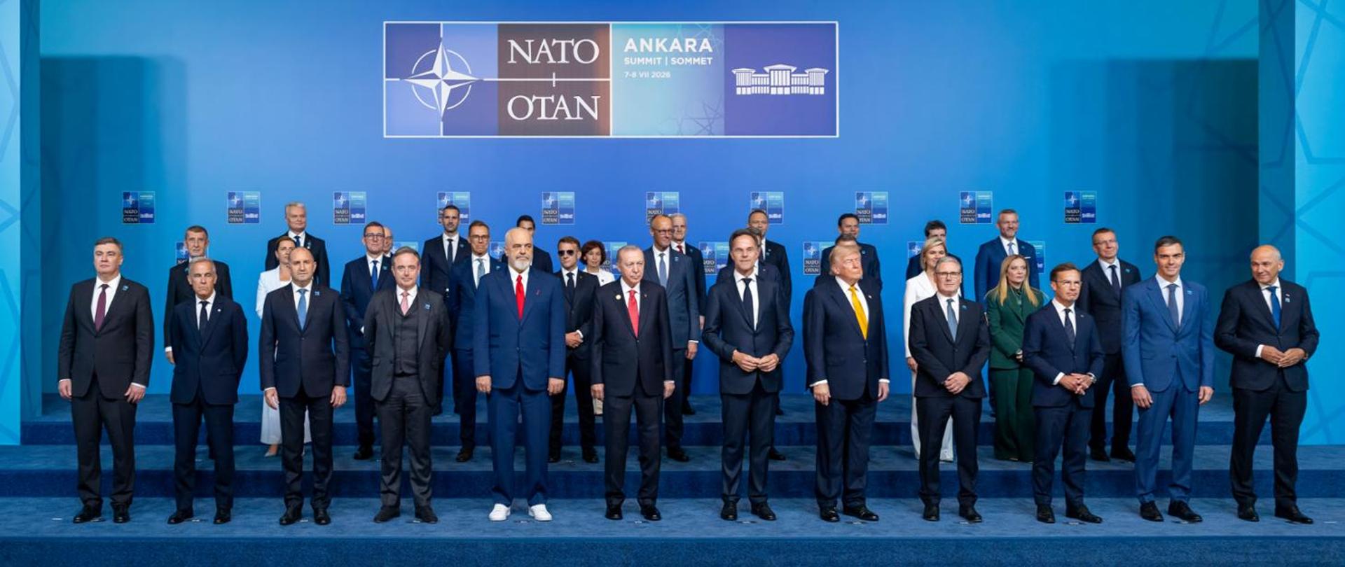 Grupowe zdjęcie uczestników szczytu NATO na tle niebieskiej sceny z logo NATO