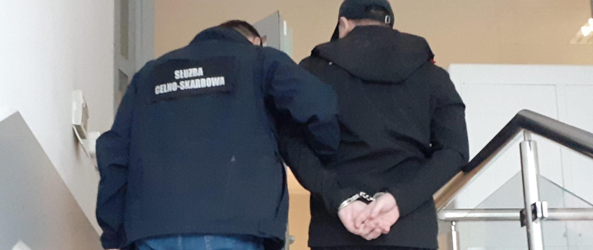 Funkcjonariusz Służby Celno-Skarbowej prowadzi zatrzymanego.