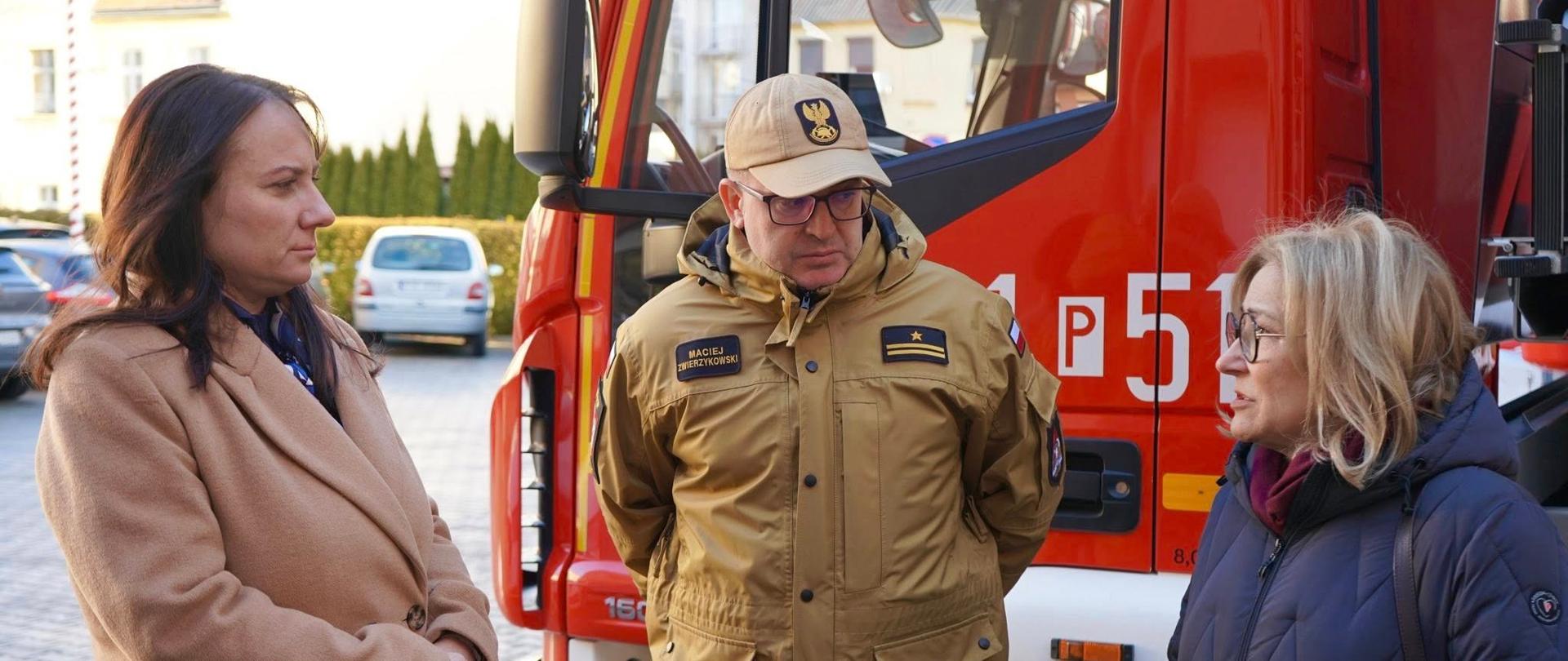 Zdjęcie przedstawia Wicewojewodę Wielkopolską, gości oraz strażaków podczas wizyty w Komendzie Powiatowej Państwowej Straży Pożarnej w Chodzieży.
W tle samochody strażackie, budynek Jednostki Ratowniczo - Gaśniczej.
