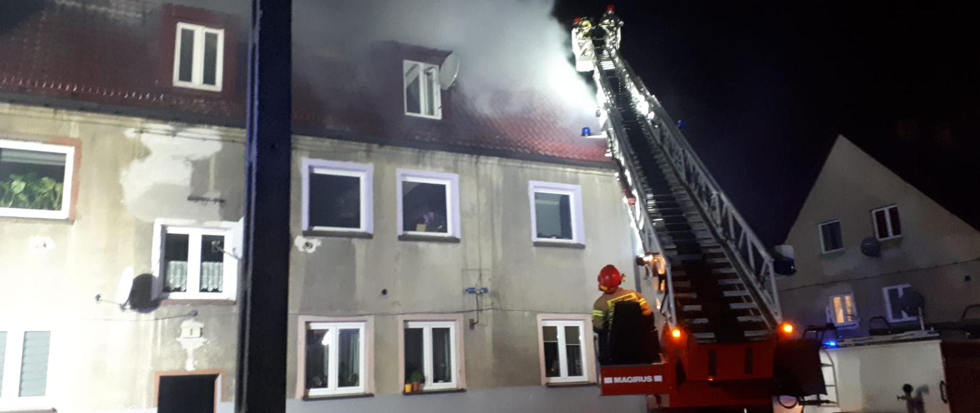 Zdjęcie przedstawia budynek przy ul. Owocowej w Rudzie Śląskiej, samochód pożarniczy oraz strażaków podczas działań gaśniczych.