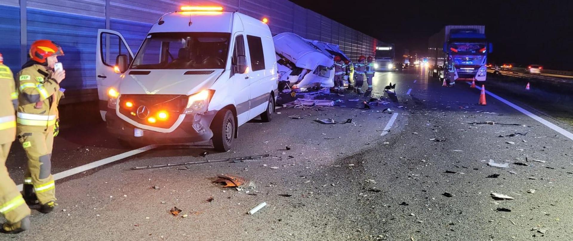 noc pas autostrady A2 na wysokości miejscowości Rozdzielna w gminie dmosin, rozbite samochody typu bus jeden należący do służby autostradowej stoją na pasie awaryjnym autostrady widoczne porozrzucane części karoserii na pasie jezdni, strażacy ratownicy dokonują ostatnich oględzin po wypadku, w tle widoczny zablokowany pas autostrady przez ciężarówki