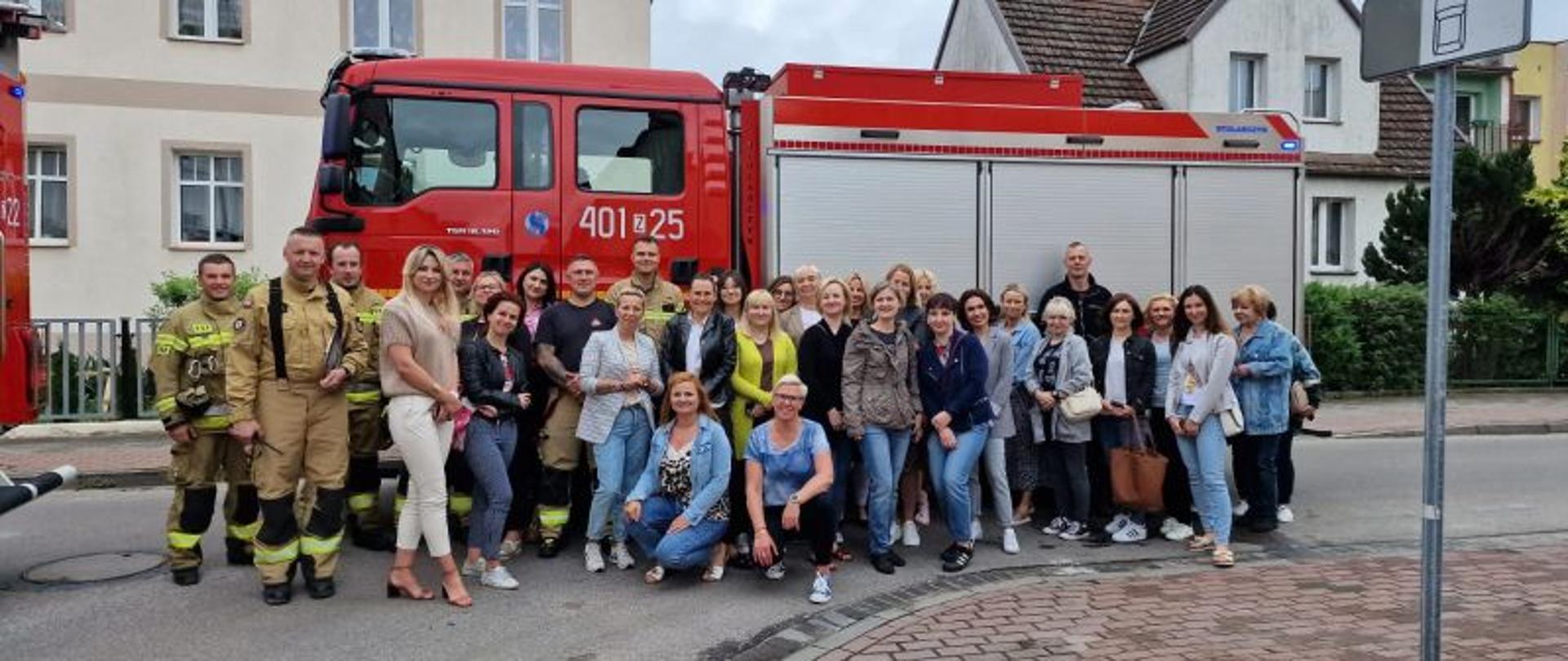 Zdjęcie grupowe pracowników i strażaków przy wozie gaśniczym.