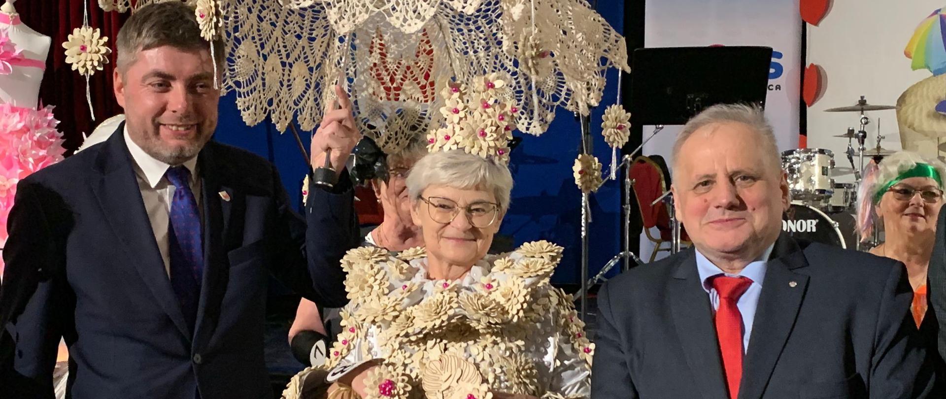 Trzy osoby w eleganckich ubraniach prezentują certyfikat, stojąc razem w radosnej atmosferze. 