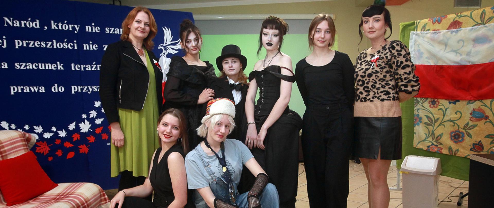 Sześć stojących i dwie kucające osoby na tle sceny z przedstawienia
