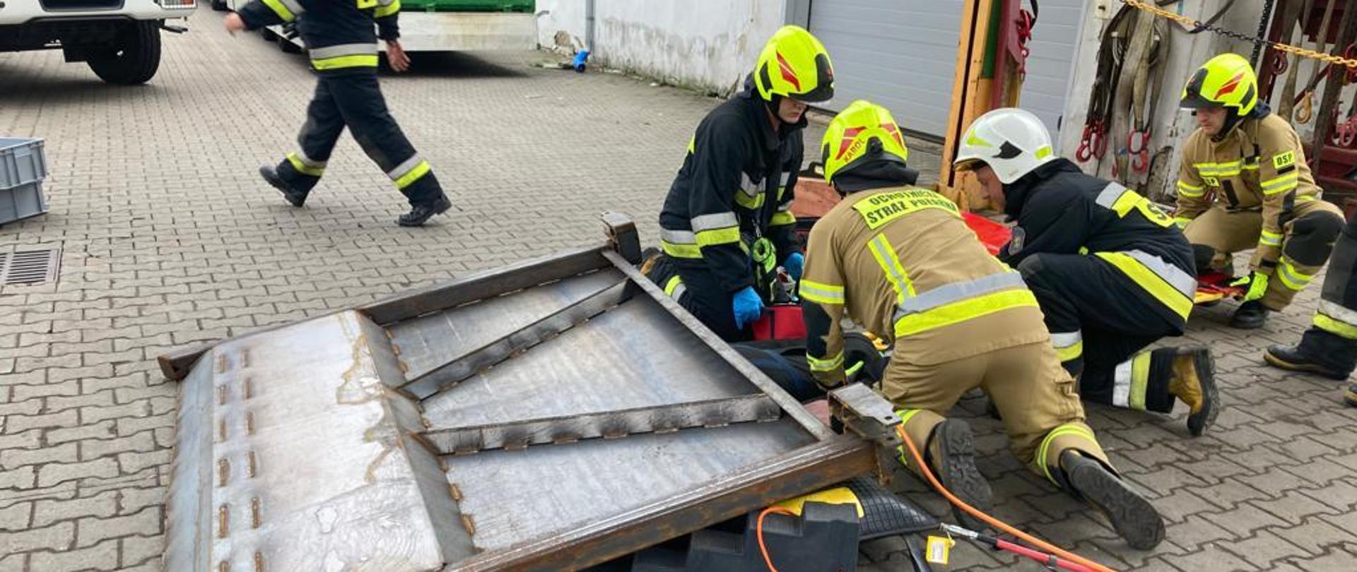 Osoba przygnieciona elementem oraz strażacy 