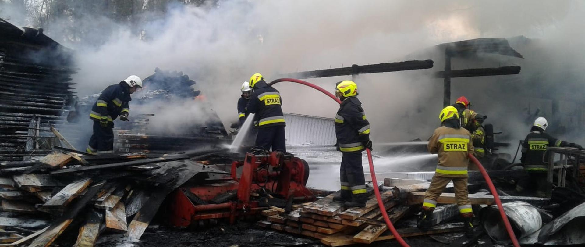 Strażacy prowadzą działania gaśnicze przy użyciu piany gaśniczej i wody stosy desek. 