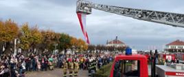 Strażacy Państwowej Straży Pożarnej oddają honor podczas śpiewania hymnu polskiego wraz z mieszkańcami miasta.