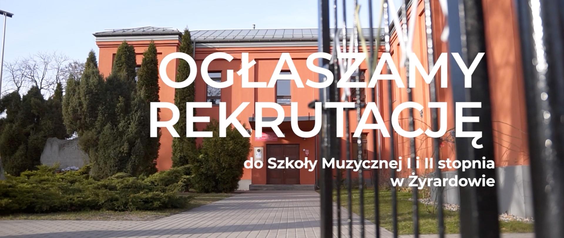 Zdjęcie przedstawiające budynek szkoły od strony ul. Narutowicza, po lewej stronie widzimy zieleniec z tujami, po prawej otwartą czarną furtkę prowadzącą do szkoły. Duży napis "Ogłaszamy rekrutację do Szkoły Muzycznej I i II stopnia w Żyrardowie" 